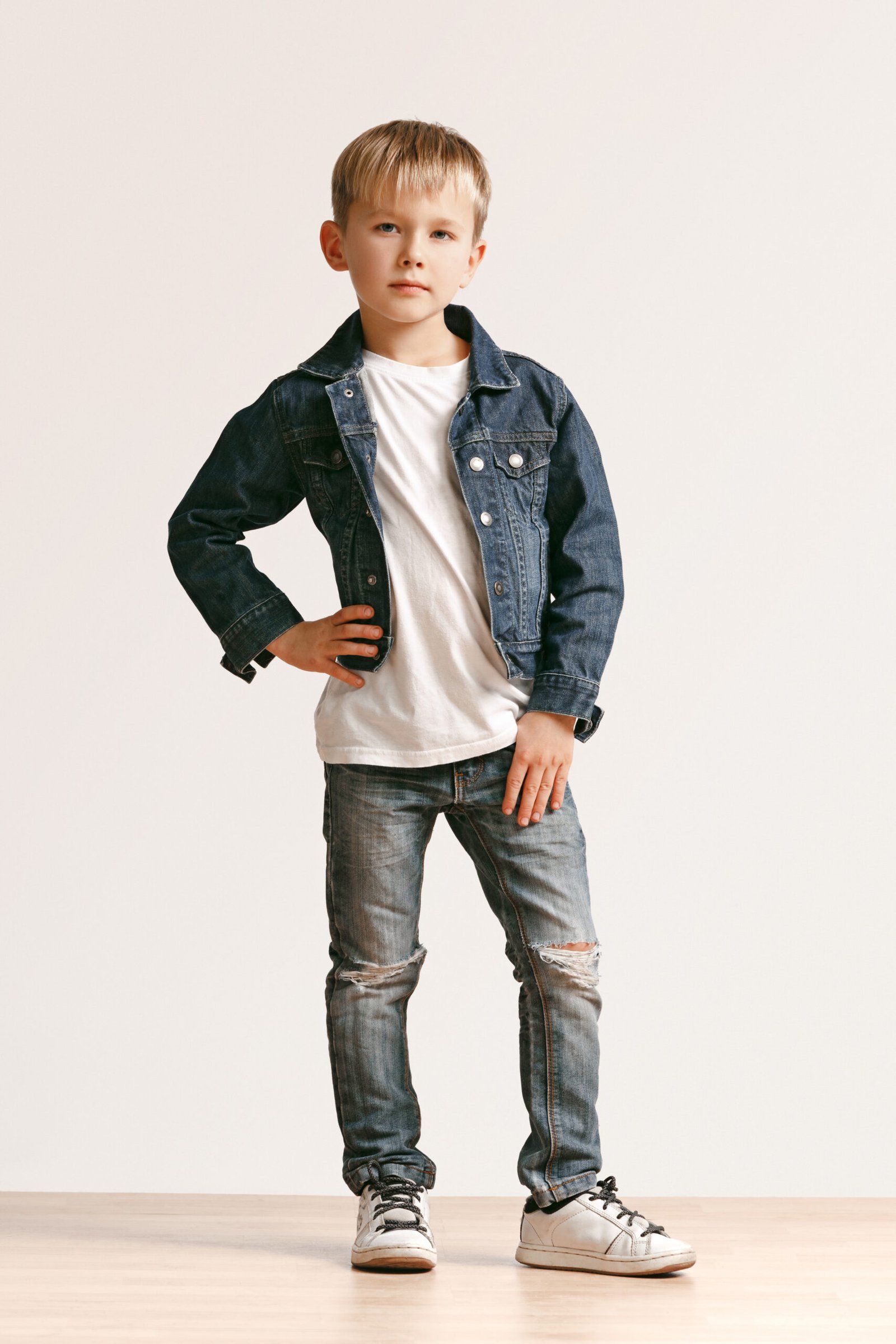 The portrait of cute little boy in stylish jeans clothes looking at camera at studio